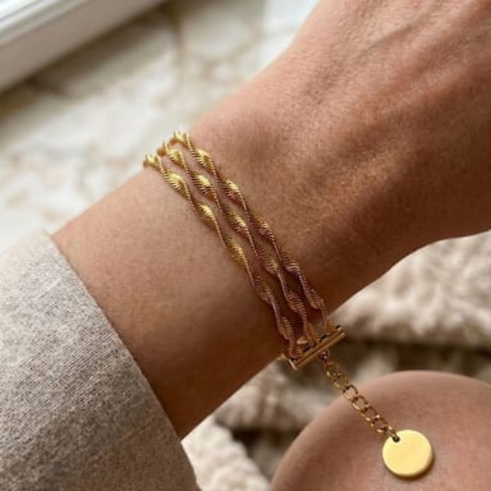 A close-up shot focusing on the justjewel.co.in triple-strand twisted rope bracelet on a woman's wrist, made with waterproof 316L stainless steel and a high-quality gold finish.
